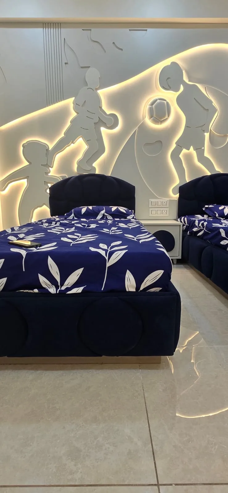 Children’s bedroom with twin upholstered beds under a backlit CNC-cut footballer mural