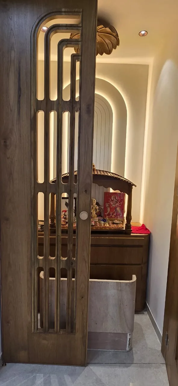 Sliding wooden jaali door to the pooja room, half open on the backlit niche